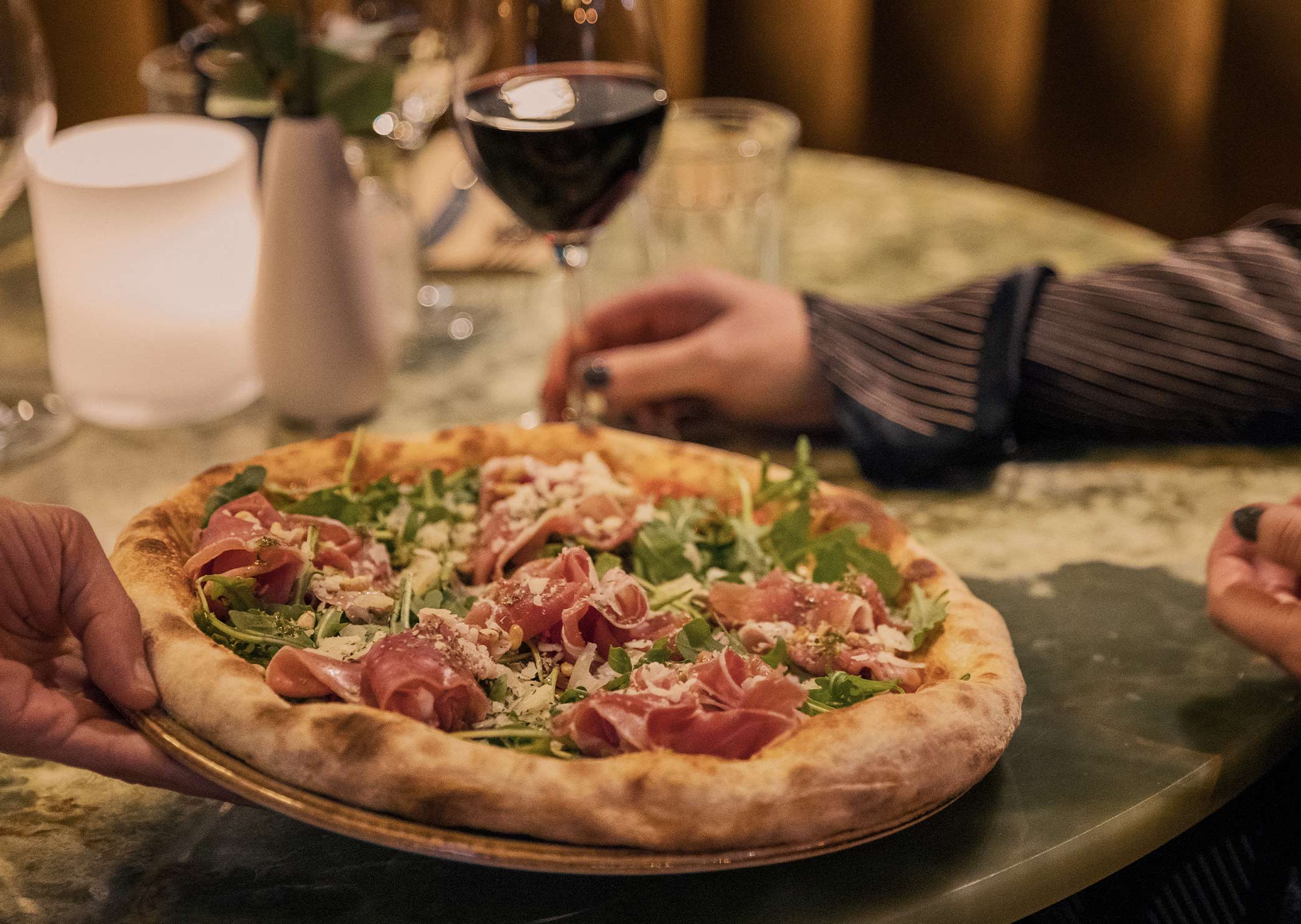 Pizza med lufttorkad skinka och ruccola serverad med ett glas rödvin på Corner.